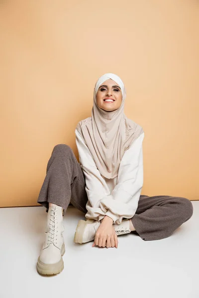 Carefree muslim woman in trendy casual outfit and hijab sitting on beige, modern lifestyle — Stock Photo