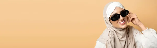 Joyeuse femme musulmane en hijab et lunettes de soleil tendance regardant la caméra sur beige, individualité, bannière — Photo de stock