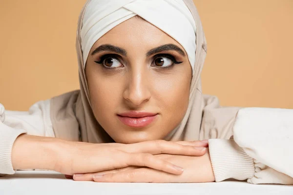 Крупним планом портрет чарівної мусульманки з макіяжем, сидячи за столом і дивлячись на бежевий — стокове фото