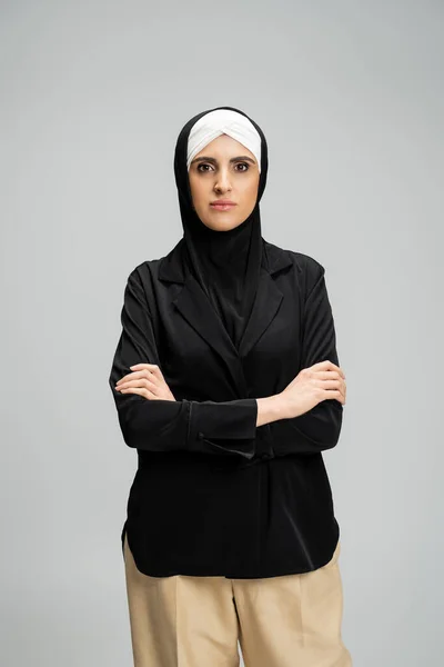 Confident muslim businesswoman in hijab and jacket standing with folded arms on grey, headshot — Stock Photo