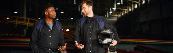 Felici uomini multiculturali che chiacchierano all'interno del circuito del kart, piloti di kart che tengono i caschi, banner — Foto stock