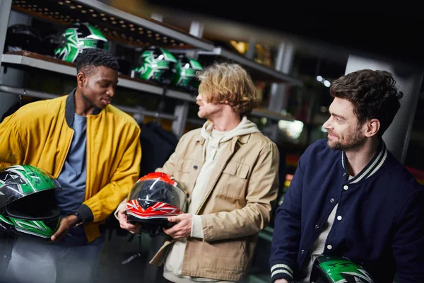 Fröhliche multikulturelle Männerfreunde in Jacken mit Helm, Indoor-Rennbahn, Kartkonzept — Stockfoto