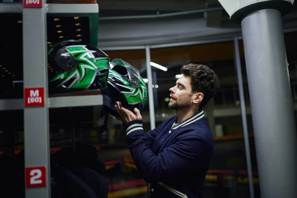 Hombre guapo elegir casco para karting dentro del vestuario de karting, concepto de automovilismo - foto de stock