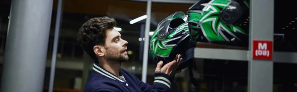 Handsome man choosing helmet for karting inside of karting locker room, motorsport concept, banner — Stock Photo