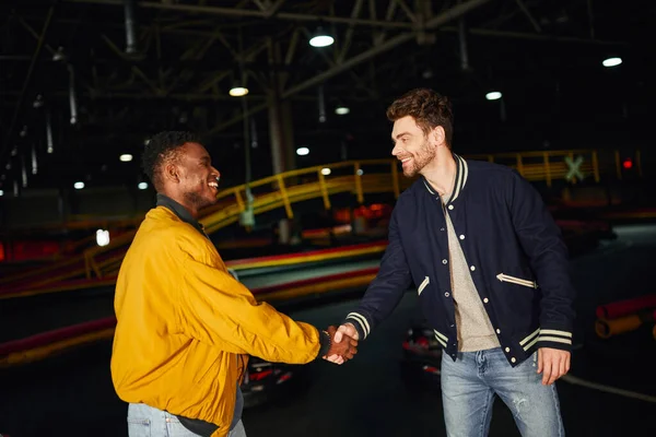 Feliz afro-americano homem apertando as mãos com amigo dentro de karting pista de corrida, competição — Fotografia de Stock