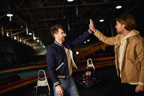 Amigos masculinos felices dando cinco altos el uno al otro dentro de pista de karting, trabajo en equipo y ganar - foto de stock