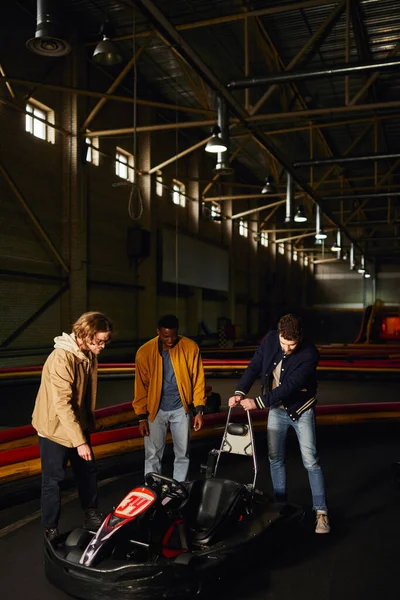 Heureux amis interracial debout près rouge go-kart à l'intérieur de la piste intérieure, passe-temps de sport automobile — Photo de stock