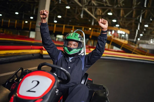 Go kart speed drive, excited african american driver in helmet raising hands and winning race — Stock Photo