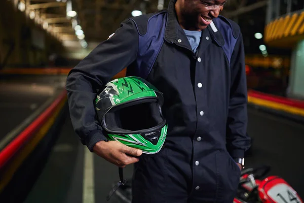 Alegre afroamericano hombre en ropa deportiva celebración casco y de pie en karting circuito de pista - foto de stock