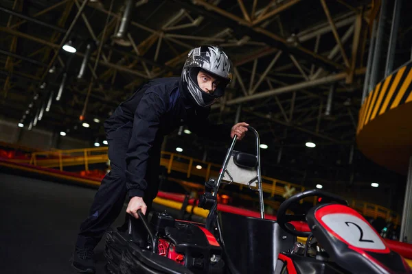 Automovilismo y velocidad, conductor de kart enfocado en casco y ropa deportiva empujando karts en circuito - foto de stock