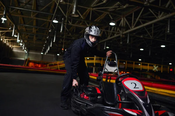 Motorsport and speed drive, focused kart driver in sportswear and helmet pushing go kart on circuit — Stock Photo