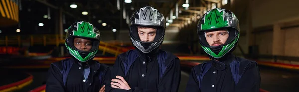 Fiduciosi piloti di go kart in abbigliamento sportivo e caschi in piedi con le braccia piegate sul circuito, banner — Foto stock
