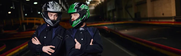 Due piloti fiduciosi di go kart in abbigliamento sportivo e caschi in piedi con le braccia piegate sul circuito, banner — Foto stock
