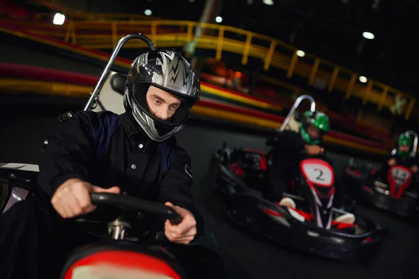 Concentrado diversos hombres en cascos de conducción ir kart en circuito cubierto, automovilismo y adrenalina - foto de stock