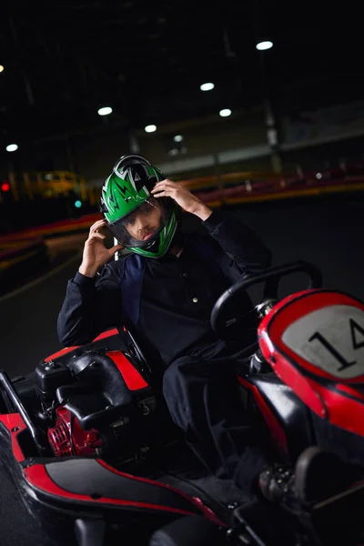 Corredor quitándose el casco y sentado en ir kart después de la carrera en el circuito interior, concepto de adrenalina - foto de stock