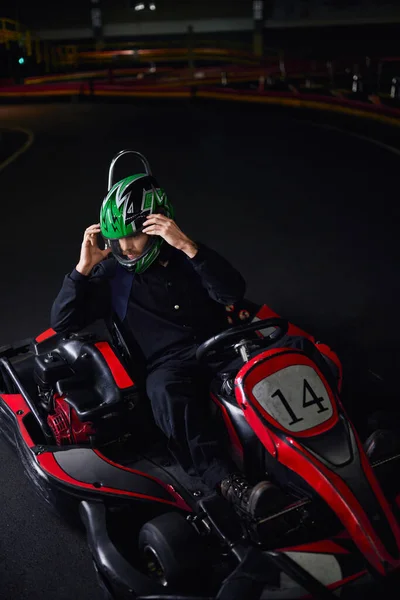 Homem tirando o capacete e sentado em go kart após corrida no circuito interno, conceito de adrenalina — Fotografia de Stock