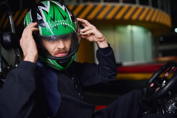 Portrait of man taking off helmet and sitting in go kart after race on indoor circuit, adrenaline — Stock Photo