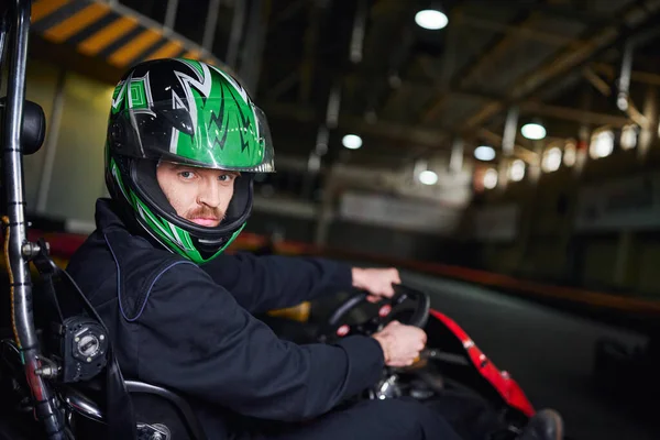 Retrato del hombre en casco y ropa deportiva conducción ir kart en circuito interior, concepto de adrenalina - foto de stock