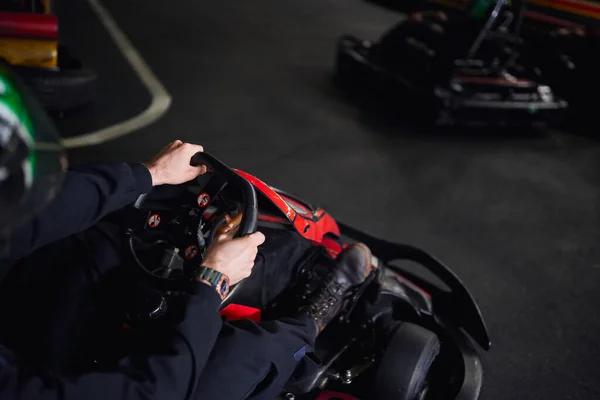 Racer in helmet and sportswear driving go kart on indoor circuit, steering wheel, adrenaline concept — Stock Photo