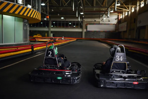 Two karting drivers in helmets and sportswear driving go kart on indoor circuit, competitors — Stock Photo