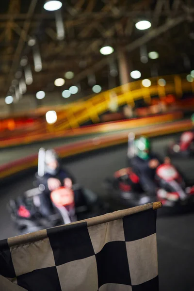 Checkered black and white racing flag next to drivers on blurred backdrop, go kart concept — Stock Photo