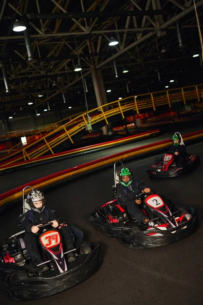 Groupe de personnes multiethniques conduisant aller kart sur circuit intérieur, course de vitesse et compétition — Photo de stock