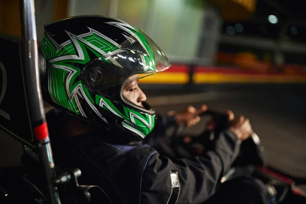 African american go cart racer in helmet driving on indoor circuit, speed racing and motorsport — Stock Photo