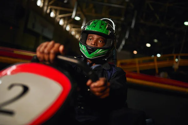 Afro-americano go cart racer em capacete dirigindo no circuito indoor, speed racing challenge — Fotografia de Stock