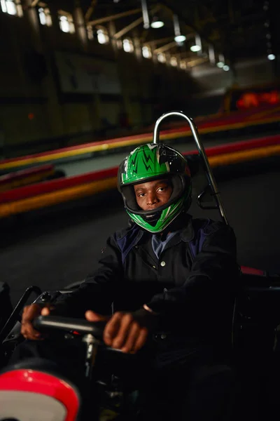 Africano americano ir kart conductor en casco de conducción en circuito interior, pista de carreras de velocidad, automovilismo - foto de stock