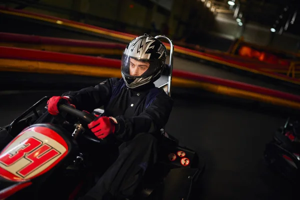 Conductor enfocado en carreras de casco en coche de karting go en circuito interior, velocidad de conducción y el concepto de automovilismo - foto de stock
