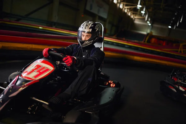 Focused speed racer in helmet driving go kart car on indoor circuit, motorsport competition concept — Stock Photo