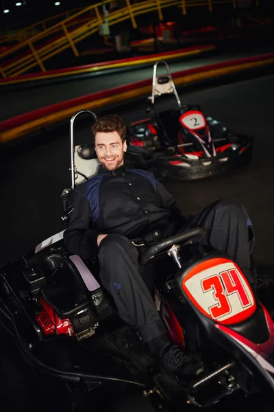 Cheerful go kart driver in sportswear sitting in racing car inside of indoor circuit, winner — Stock Photo