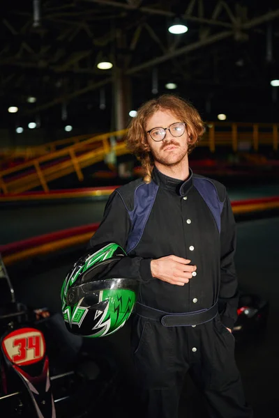 Ir conductor de kart en gafas y ropa deportiva de pie con casco dentro de la pista de carreras, circuito - foto de stock