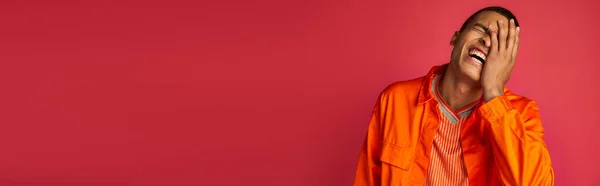 Animado afro-americano cara rindo e obscurecendo rosto em vermelho, camisa laranja, banner, espaço de cópia — Fotografia de Stock
