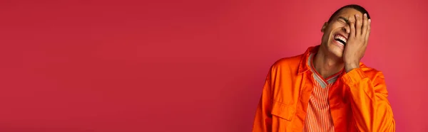 Excited african american guy laughing and obscuring face on red, orange shirt, banner, copy space — Stock Photo