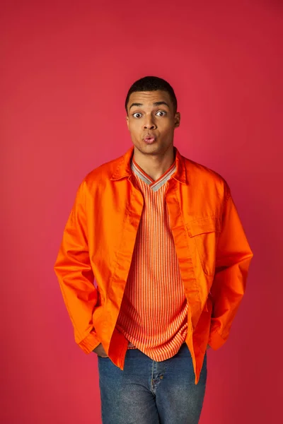 Desanimado afro-americano homem amuado lábios e olhando para a câmera em vermelho, camisa laranja, elegante — Fotografia de Stock