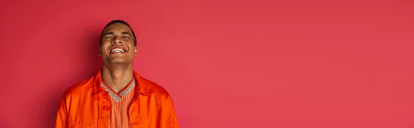 Ragazzo afroamericano eccitato ridere con gli occhi chiusi su rosso, camicia arancione, banner, spazio copia — Foto stock