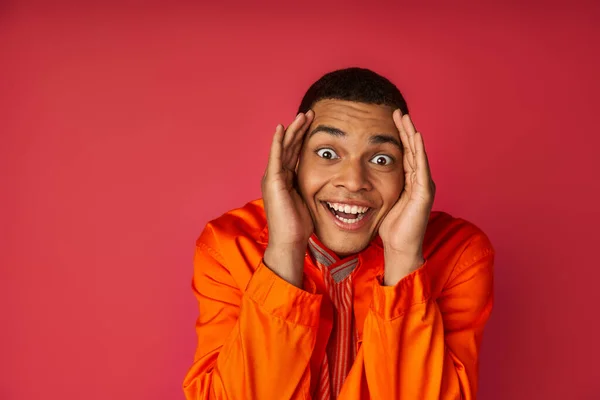 Homem americano africano super alegre em camisa laranja, com as mãos perto do rosto olhando para a câmera no vermelho — Fotografia de Stock
