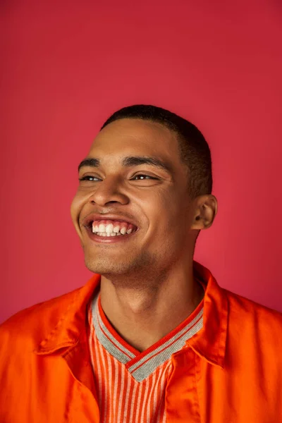 Retrato de un joven afroamericano con sonrisa radiante, elegante camisa naranja, fondo rojo - foto de stock
