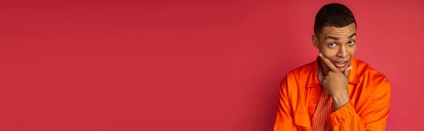 Nachdenklicher und angespannter afrikanisch-amerikanischer Mann in orangefarbenem Hemd blickt in die Kamera auf rot, Banner, Kopierraum — Stockfoto
