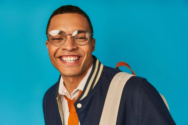 Pleased african american student in eyeglasses and trendy jacket smiling at camera on blue, portrait — Stock Photo