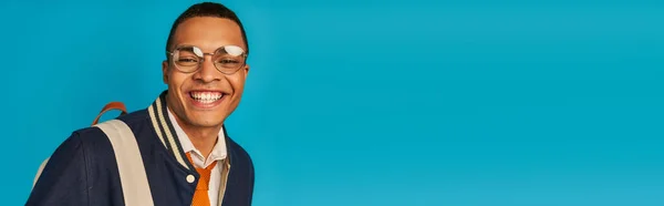 Glücklich afrikanisch-amerikanischer Student in stylischer Jacke und Brille auf blau, Banner, Kopierraum — Stockfoto