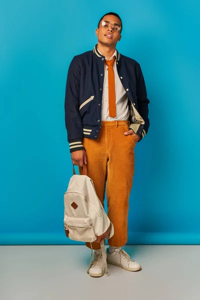 Confident african american student in trendy casual clothes with backpack and hand in pocket on blue — Stock Photo