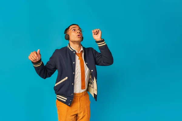 Excited and trendy african american student in wireless headphones dancing on blue — Stock Photo