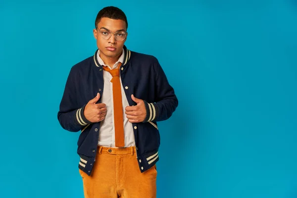 Confident african american student in trendy jacket and orange pants looking at camera on blue — Stock Photo