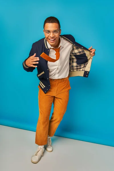 Confident african american student with trendy clothes and radiant smile looking at camera on blue — Stock Photo