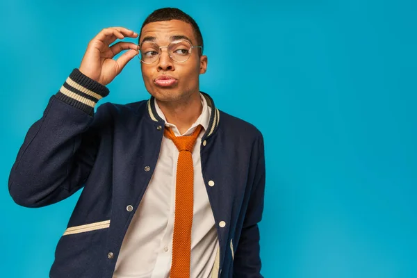 Surpris étudiant afro-américain ajuster les lunettes, bouder les lèvres et regarder loin sur le bleu — Photo de stock