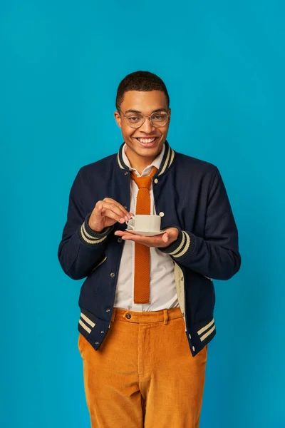 Étudiant afro-américain à la mode avec tasse de café et sourire radieux en regardant la caméra sur bleu — Photo de stock