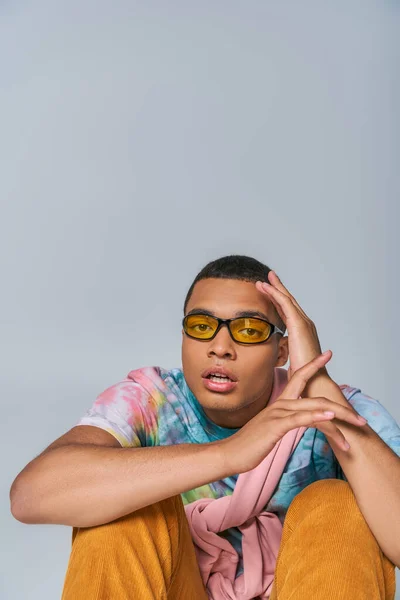 Youthful african american man in trendy sunglasses and tie-dye t-shirt looking at camera on grey — Stock Photo