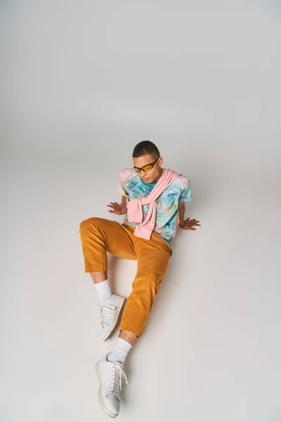 Uomo afroamericano in pantaloni arancioni, cravatta-tintura t-shirt, occhiali da sole seduto su grigio, vista ad alto angolo — Foto stock